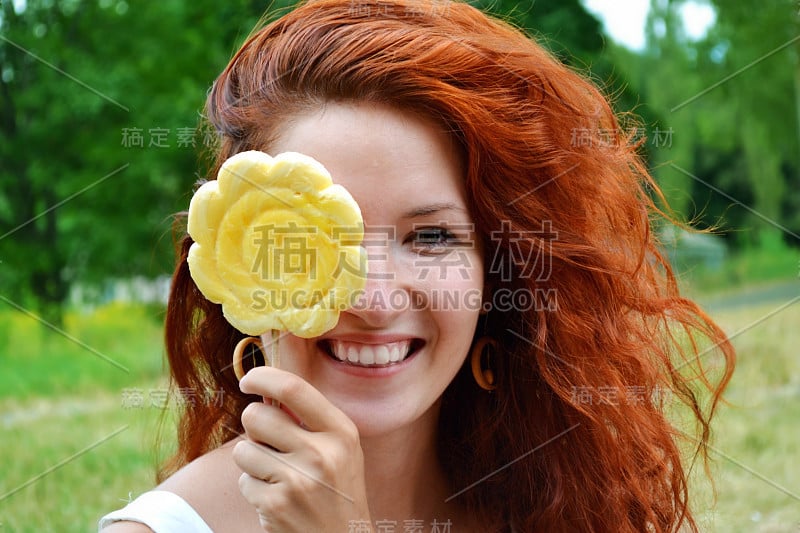 漂亮的年轻红发女人开心地笑着拿着黄色的棒棒糖