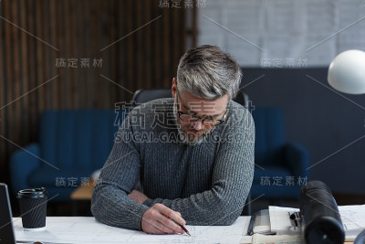 室内设计师在办公室工作与蓝图。工程师检查建筑平面图，为建筑工程画草图。英俊的胡子男人在工作场所的肖像