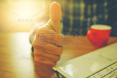 竖起大拇指，桌上放着笔记本电脑和咖啡杯