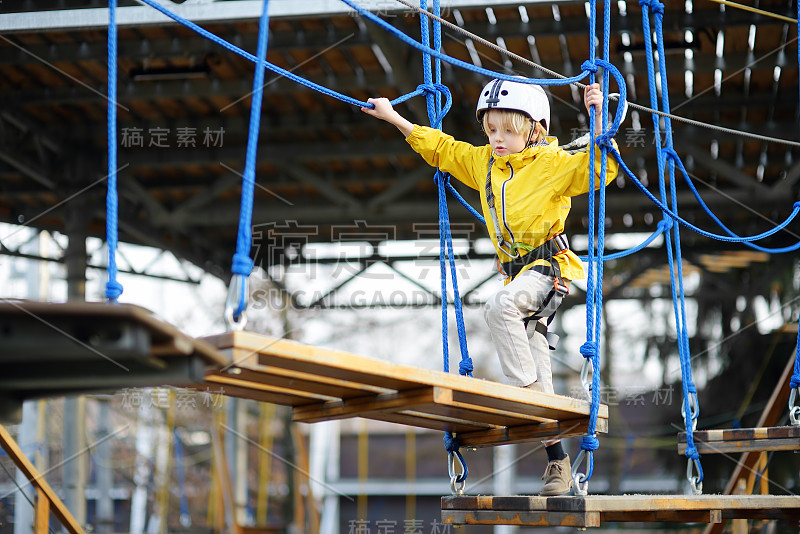 小男孩在冒险公园里玩耍，在绳索、楼梯、桥之间。公园内的户外攀岩探险游乐场。儿童活动娱乐