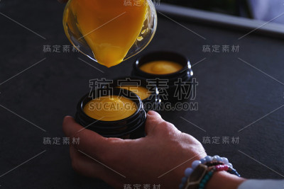 女性双手将新鲜制作的天然diy护肤霜倒入黑色豪华玻璃瓶
