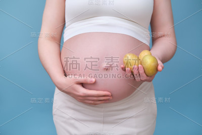 一名孕妇手里拿着三个土豆，背景是蓝色的