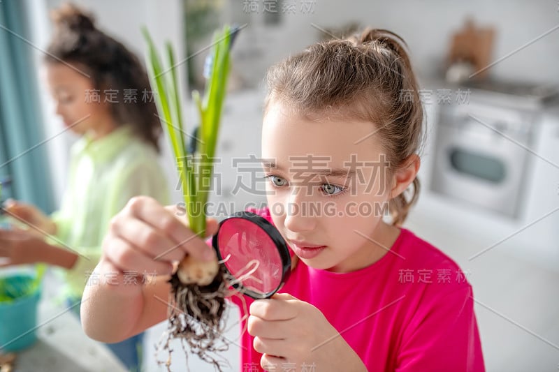 女孩手拿放大镜检查花根。