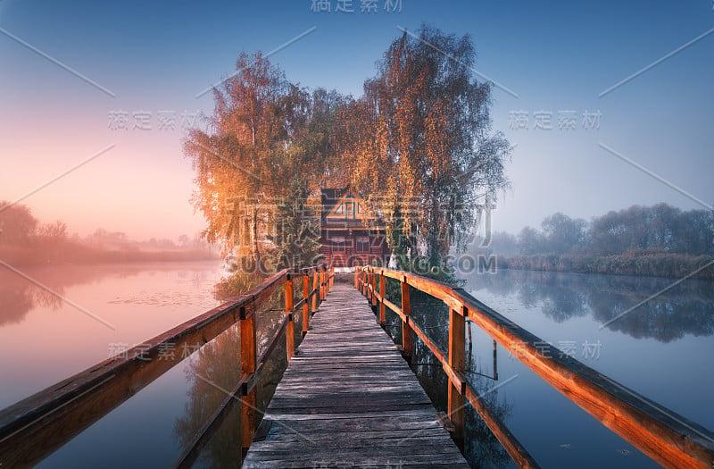 秋日清晨，有雾的老渔屋和木码头。美丽的风景与房子在小岛屿上的湖在雾，彩色的树木，码头，在水的倒影在拂