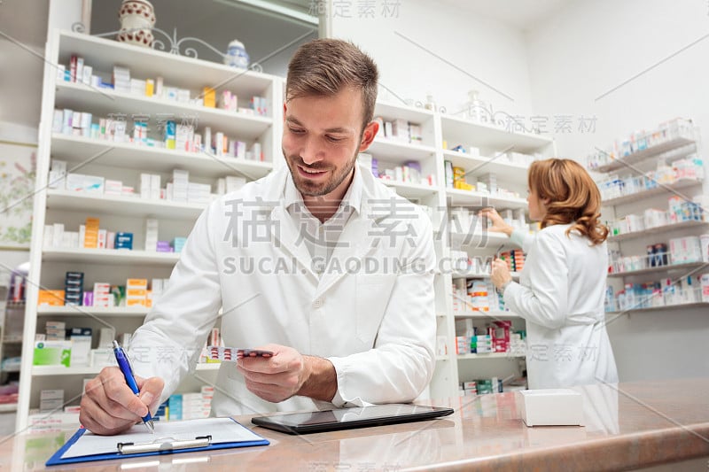 年轻的男药剂师站在药店的柜台后面，在写字板上写着什么