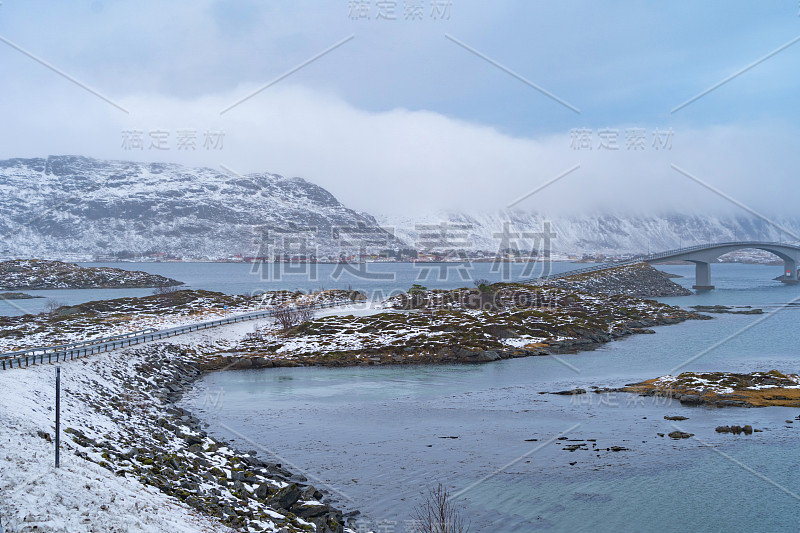 欧洲挪威诺德兰郡罗弗敦群岛的弗雷德旺大桥和公路。白雪皑皑的山峦和树木，是冬季自然景观的背景。著名的旅