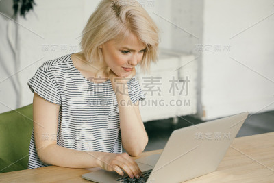 微笑的年轻女子坐在笔记本电脑前。手机在她身边