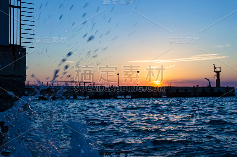 灿烂的夕阳下的大海和码头与波浪溅起的水花。