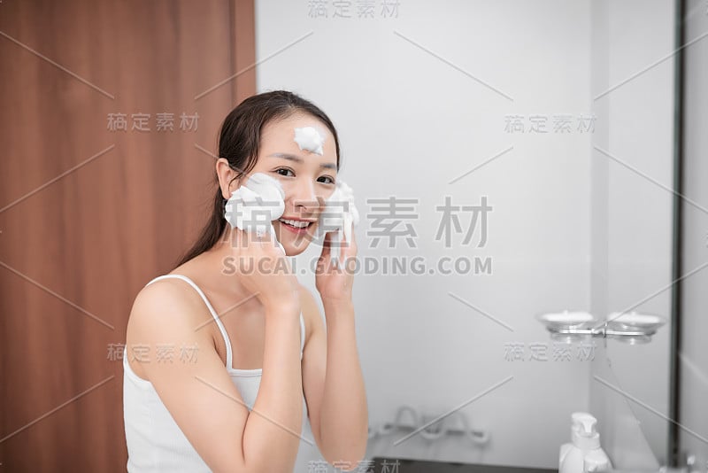 快乐美丽的女士在浴室里用肥皂洗脸