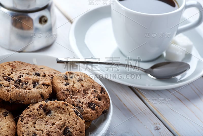 甜早餐或零食的特写照片。木质的白色盘子桌上放着巧克力和香草饼干，还有一杯黑咖啡。