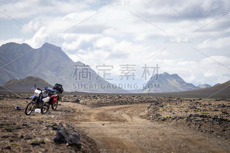 两辆摩托车站在被群山环绕的沙漠土路上，冰岛。越野旅行概念，耐力骑手装备，极端的生活方式