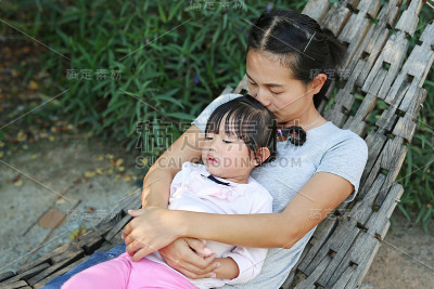 母亲和小女孩躺在花园里的木摇篮上。