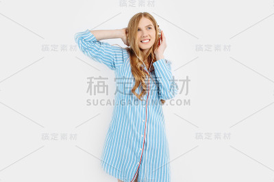 快乐迷人的年轻女孩穿着睡衣听音乐耳机上的白色背景