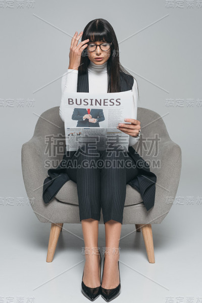 迷人的黑发女商人在灰色阅读报纸