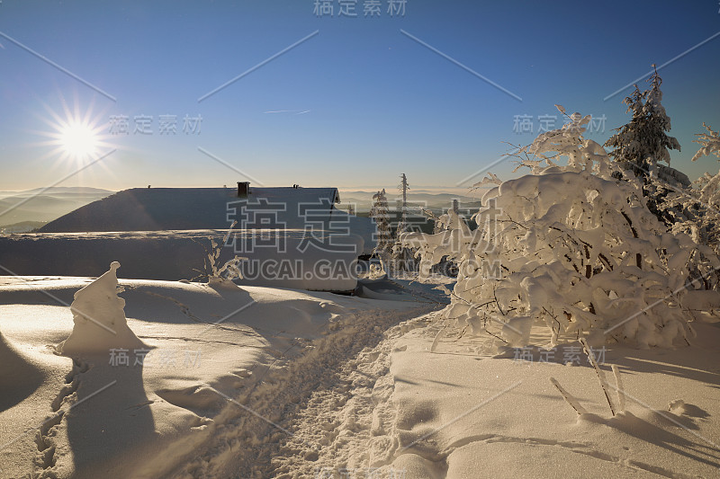 在阳光明媚的日子里，山上的小屋覆盖着白雪。