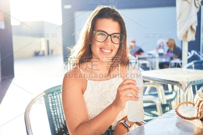 年轻漂亮的女人坐在餐厅里喝着一瓶水享受暑假
