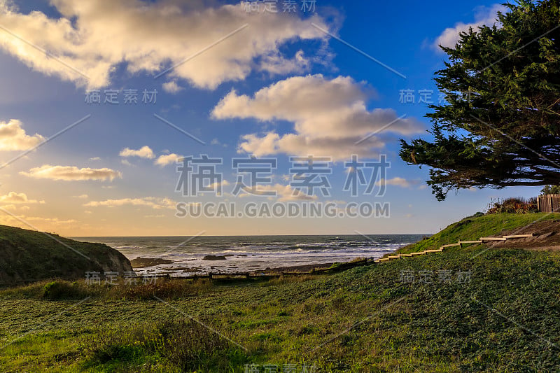 在一个多云的日子日落前，在旧金山附近莫斯海滩的绿色山丘的后面的一个太平洋和加利福尼亚海滩