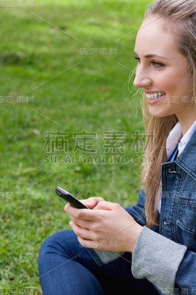 一个微笑的年轻女子坐在公园里发短信