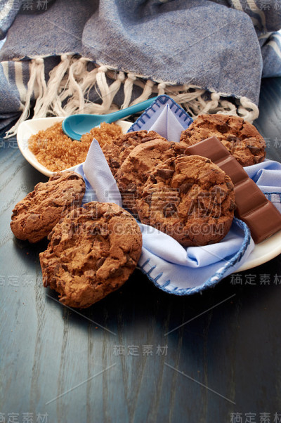 一盘可可饼干、棕甘蔗糖和巧克力，餐巾、木桌、桌布和勺子上有蓝色调