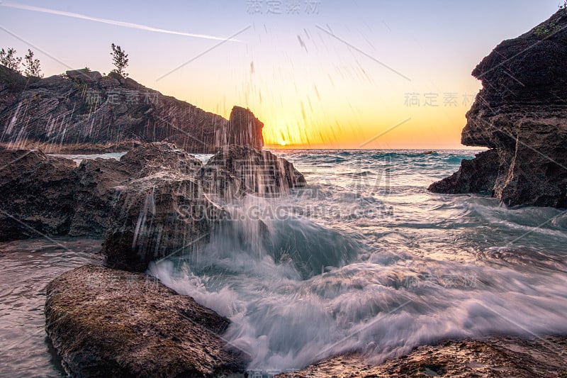 水珠从大浪中溅起，冲击着岩石海岸。太阳刚好在地平线上的背景上