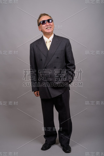 在灰色的背景下，成熟的亚洲商人戴着太阳镜看起来很酷