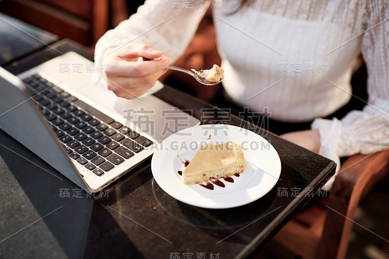 在咖啡馆里用笔记本电脑吃蛋糕的快乐女人。