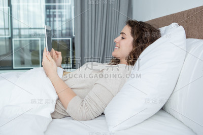 积极的年轻女子躺在床上与平板电脑