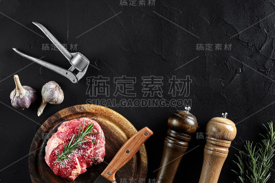 牛柳片，用刀切肉，调味料-迷迭香，胡椒，盐，大蒜。旧木板上的石头黑色桌子