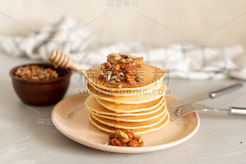 一堆美味的煎饼，上面有巧克力、蜂蜜、坚果和香蕉片，还有餐巾放在木制的背景上