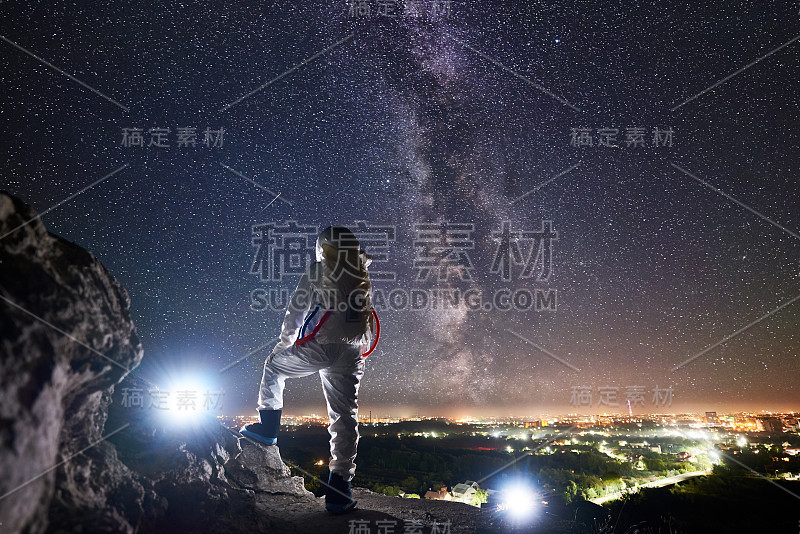 宇航员站在岩石山上看着夜空。