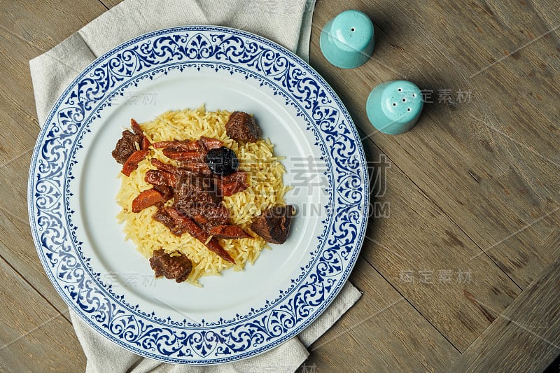 清淡的肉饭，配牛肉和胡萝卜，白色的盘子，木质的背景。带有文本拷贝空间的俯视图。传统的东方美食