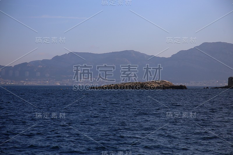 广阔的大海和岩石在前景和城市在海岸边的背景，国家公园Calanques，马赛，法国