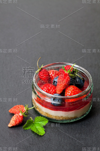 迷你野生森林浆果芝士蛋糕在玻璃锅上的黑色石头背景
