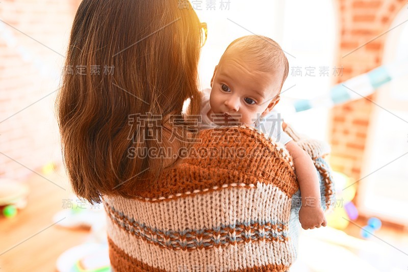 年轻漂亮的女人和她的孩子站在家里。母亲抱着新生儿