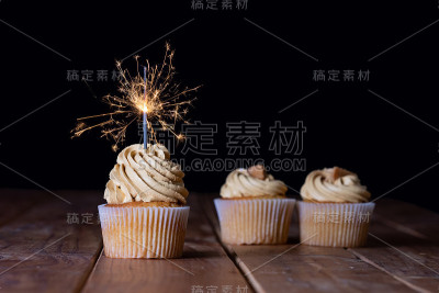三个纸杯蛋糕放在一张桌子上，黑色背景，闪闪发光