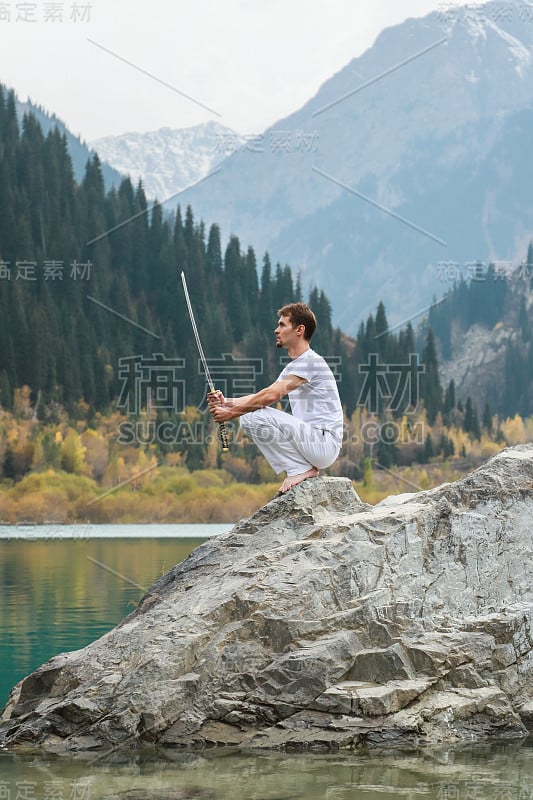 一个聪明人坐在石头上，手里拿着一把剑。山湖背景