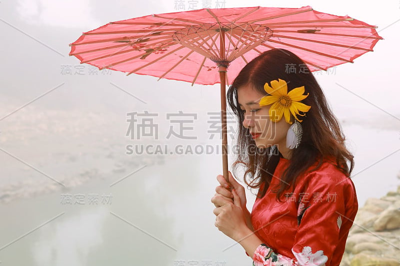 美丽的年轻亚洲妇女穿着传统的红色衣服和红色雨伞