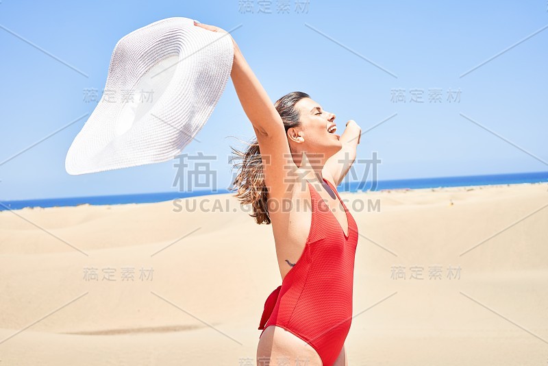 年轻美丽的女人日光浴与开放的双臂穿着夏天的swinsuit在maspalomas沙丘bech