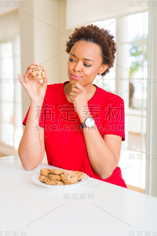 年轻的非裔美国妇女吃着巧克力片饼干严肃地面对思考问题，非常困惑的想法