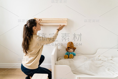 少妇在新房里装修孩子房。木制书架。中性的托儿所