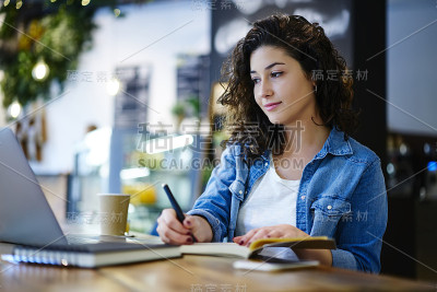 沉思的女性文案穿着时髦的服装，在连接4G网络的笔记本电脑上观看网络视频，坐在咖啡店里写笔记