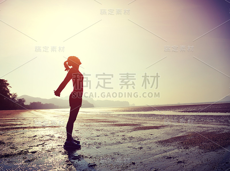 年轻的健身女人跑步伸展手臂在日出的海滩