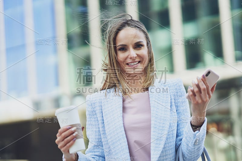 成年美女拿着智能手机在城市里行走