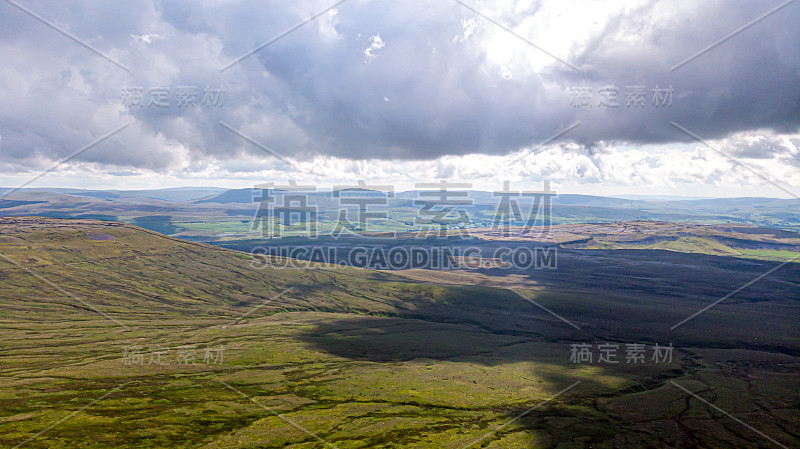 这是一个山谷的鸟瞰图，以绿色的斜坡和山脉为背景，在雄伟的蓝天和巨大的海拔白云