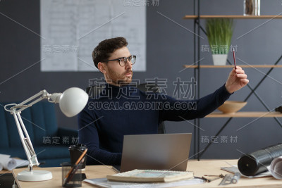 建筑师使用笔记本电脑在办公室工作。工程师对建筑方案进行思考，为建设项目寻找新的思路。长着胡须的英俊男