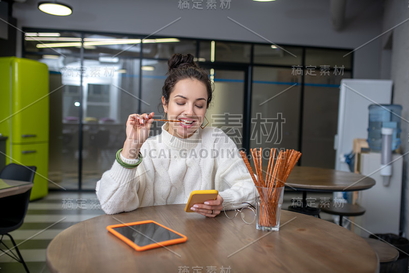 年轻女子嚼着面包棒，查看着手机