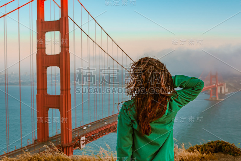 日落时分，旧金山，一位身穿绿色帽衫的年轻女子站在小山上俯瞰金门大桥