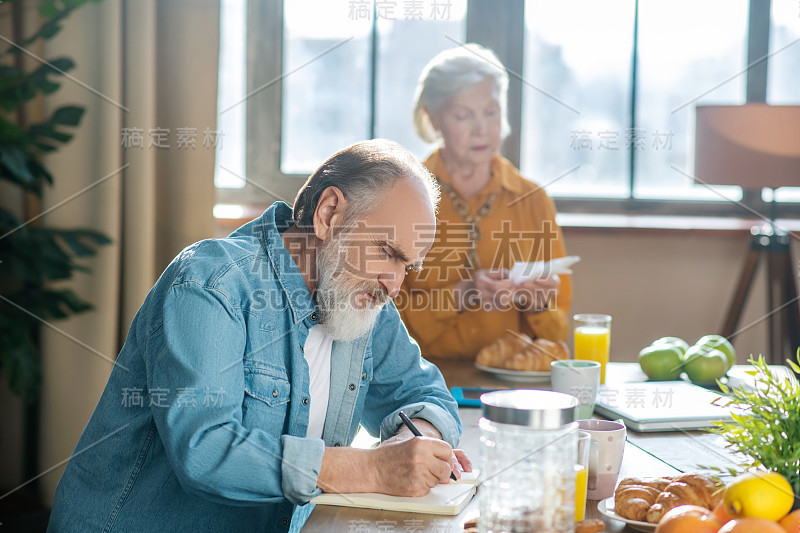 胡子花白头发的男人坐在桌子边做笔记