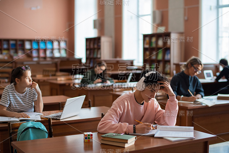 一群当代大学生坐在图书馆书桌旁