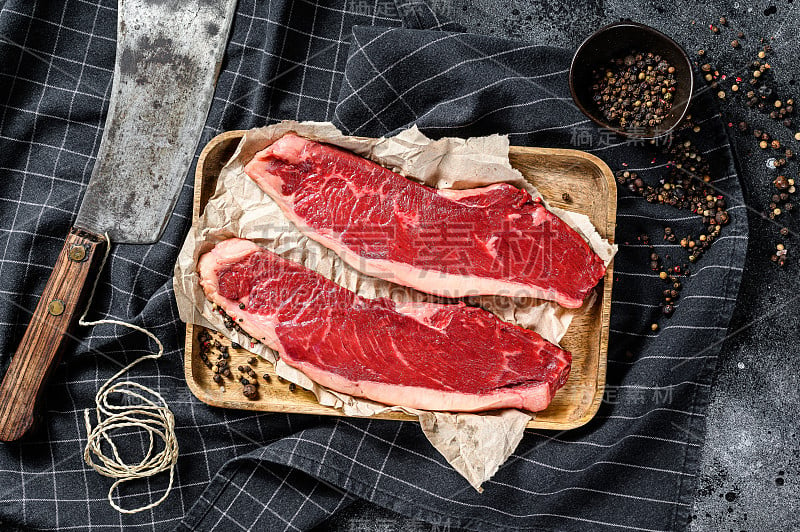 木托盘上的生西冷牛排和切肉刀。大理石牛肉。黑色背景。俯视图